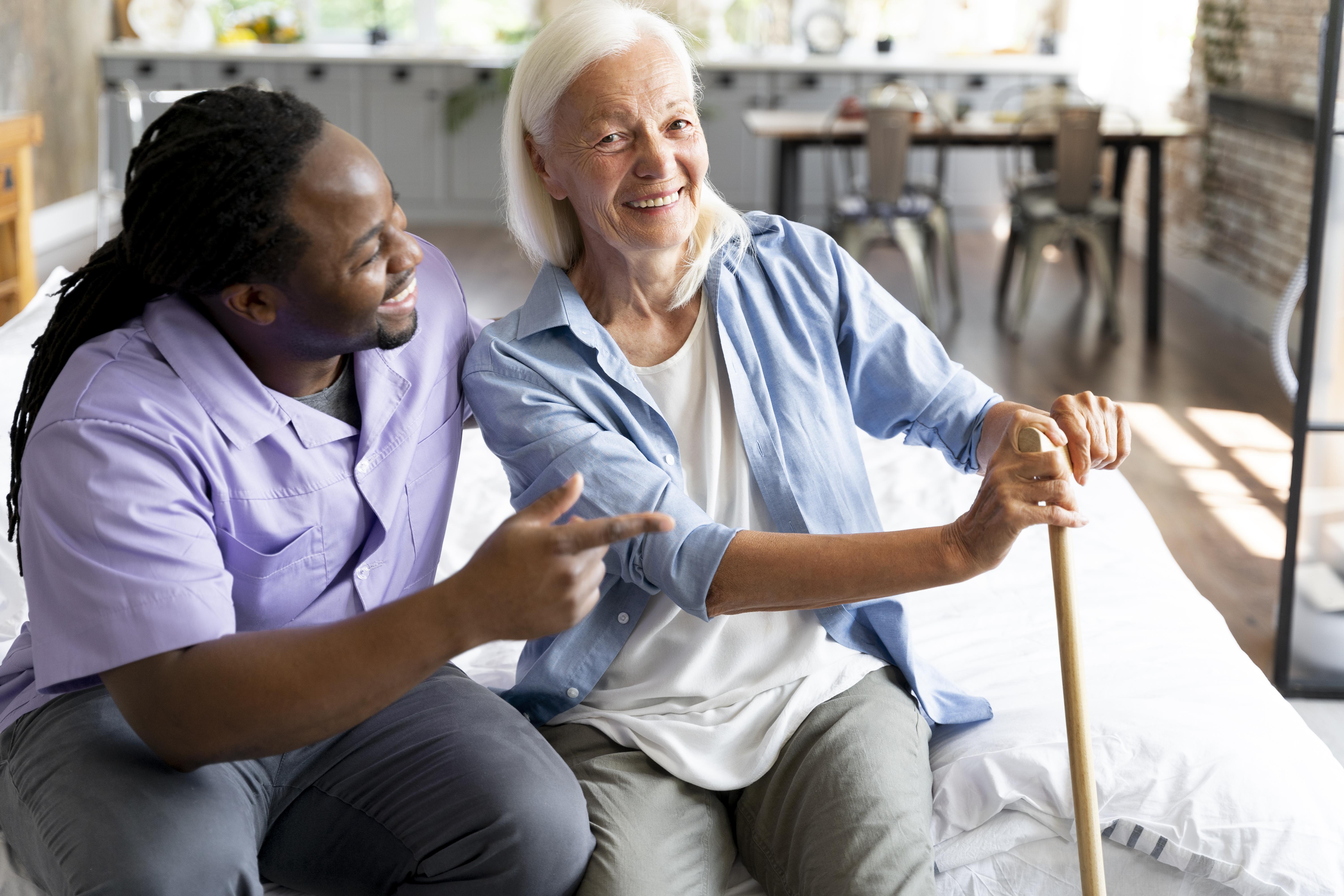 male carer serving tea to a woman sitting on a couch holding a cup of tea