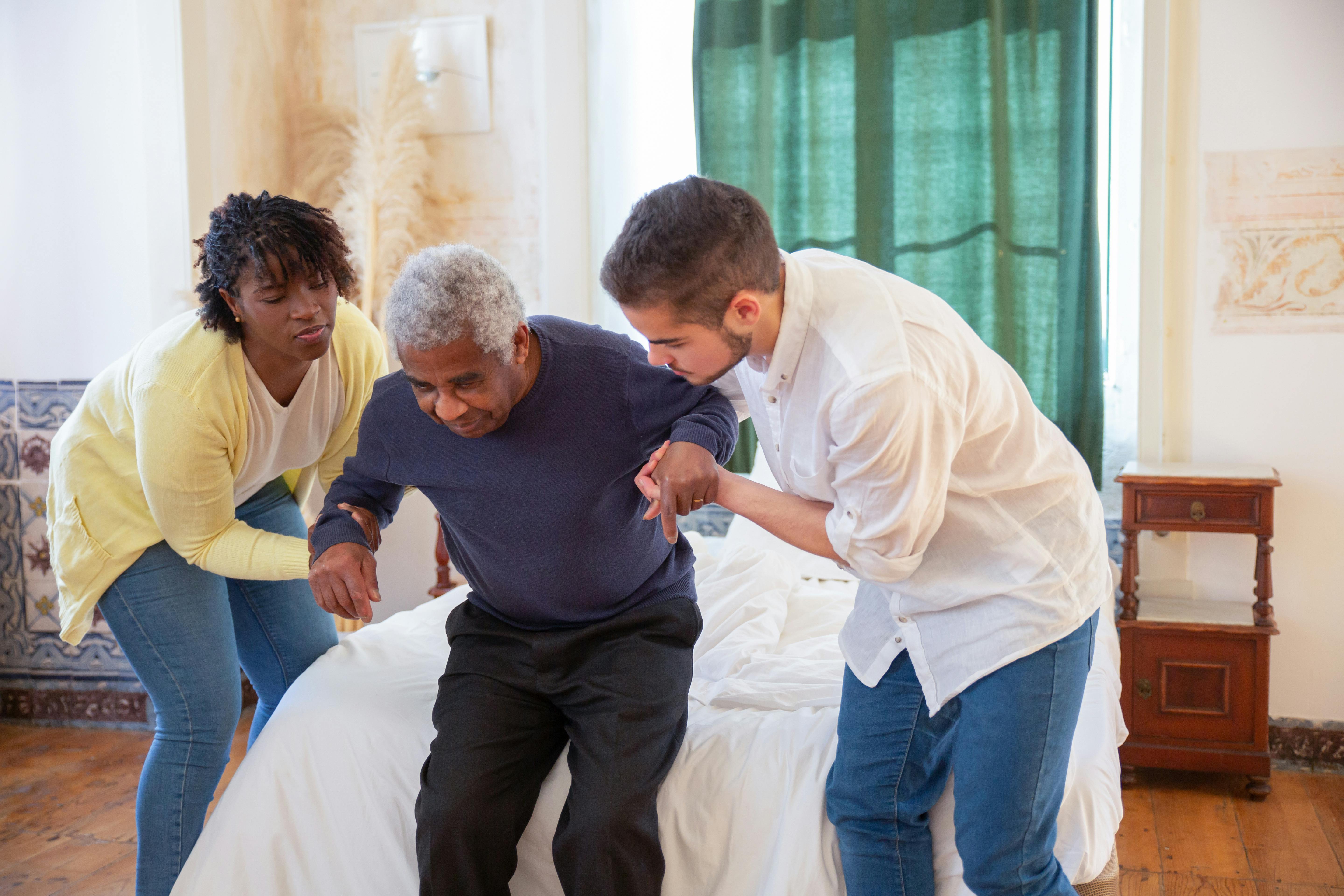 male carer checking a medical device on an elder woman's wrist while both are seated on a couch