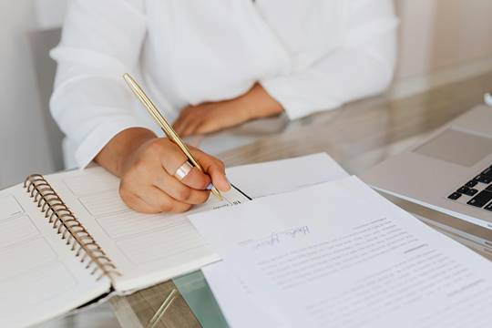 A below-face close view of a woman's writing in a notebook with a golden pen